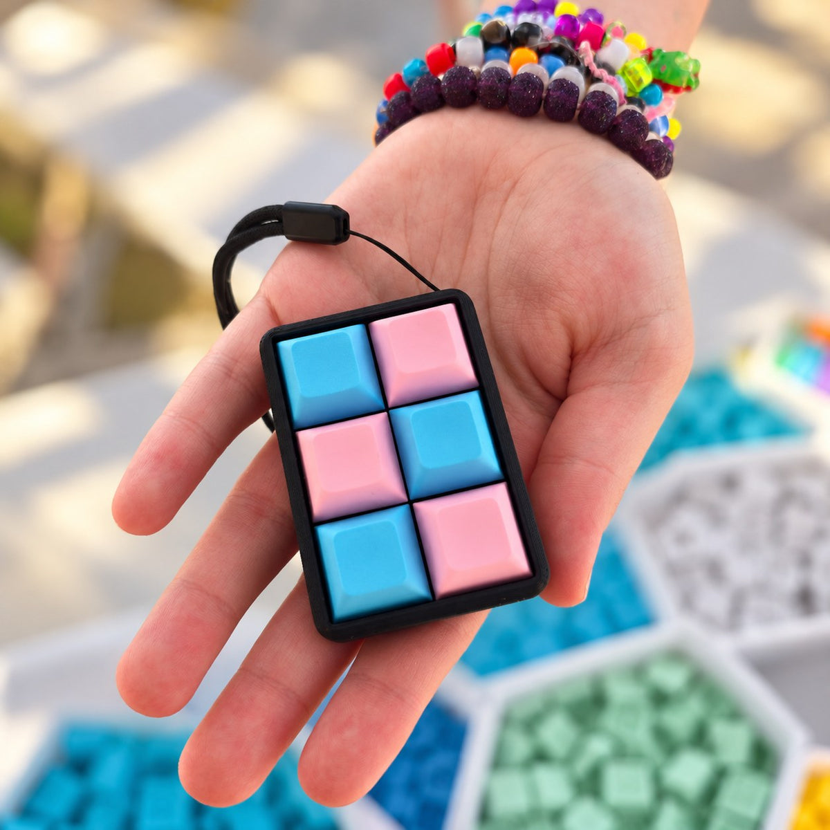 A pink and blue six-key keyboard fidget resting in a hand, showing its size.