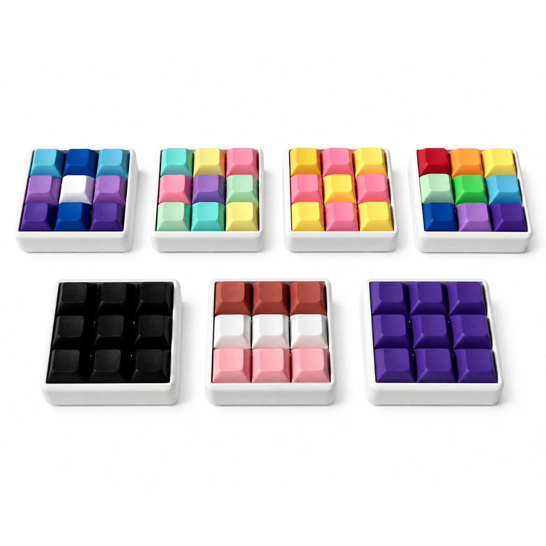 Angled view of seven Original 9-key square keyboard fidgets with white bases in different keycap color combinations.