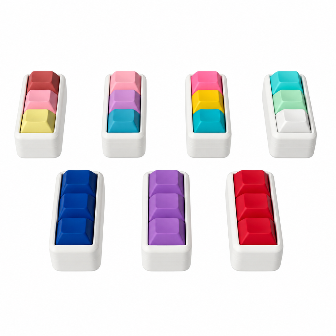 Seven Mini 3-key keyboard fidgets with white bases, shown at an angle in all available color combinations.