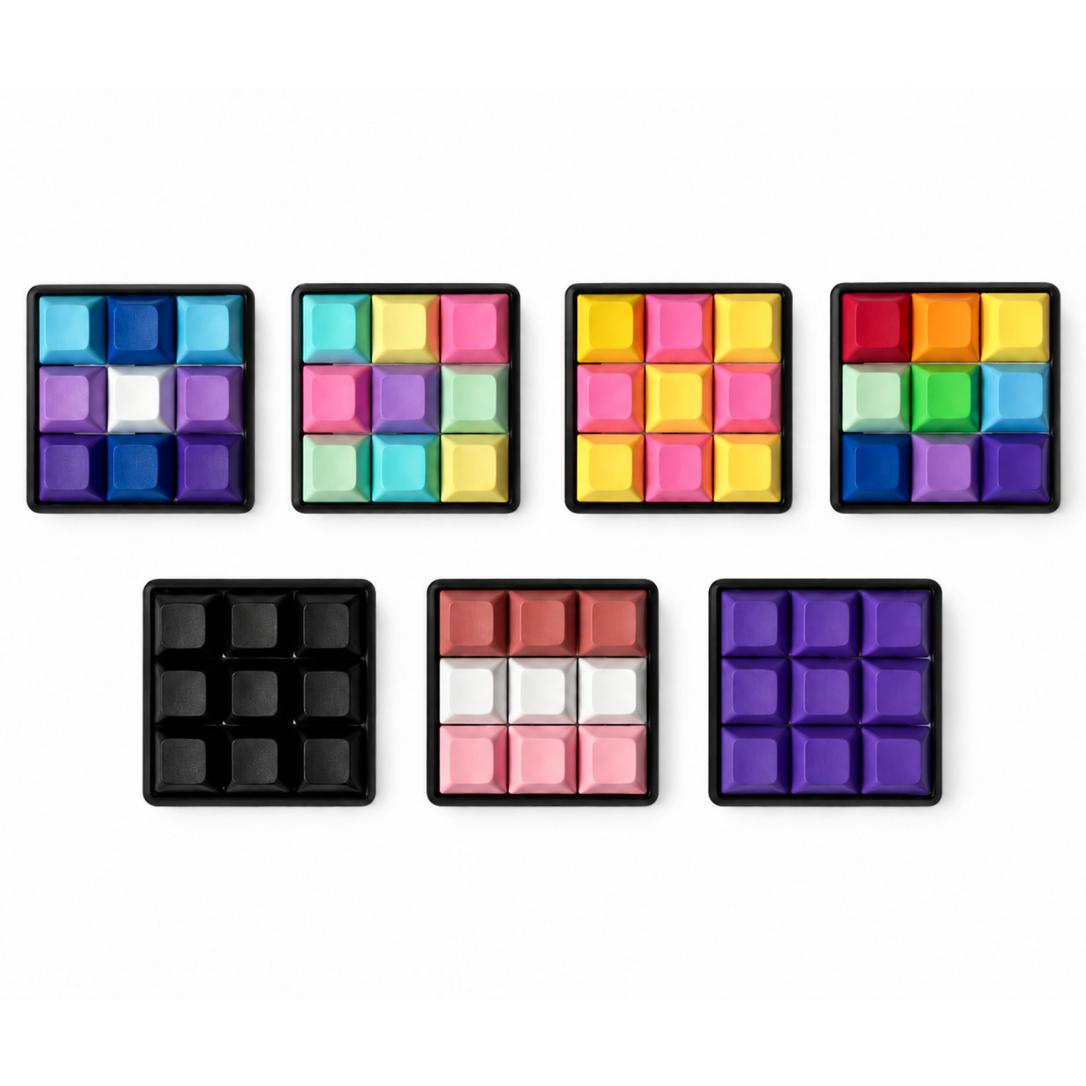 Top view of seven Original 9-key square keyboard fidgets with black bases in different keycap color combinations.