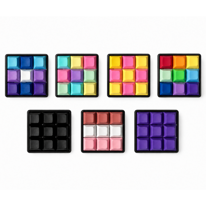 Top view of seven Original 9-key square keyboard fidgets with black bases in different keycap color combinations.
