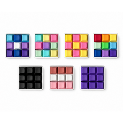 Top view of seven Original 9-key square keyboard fidgets with white bases in different keycap color combinations.